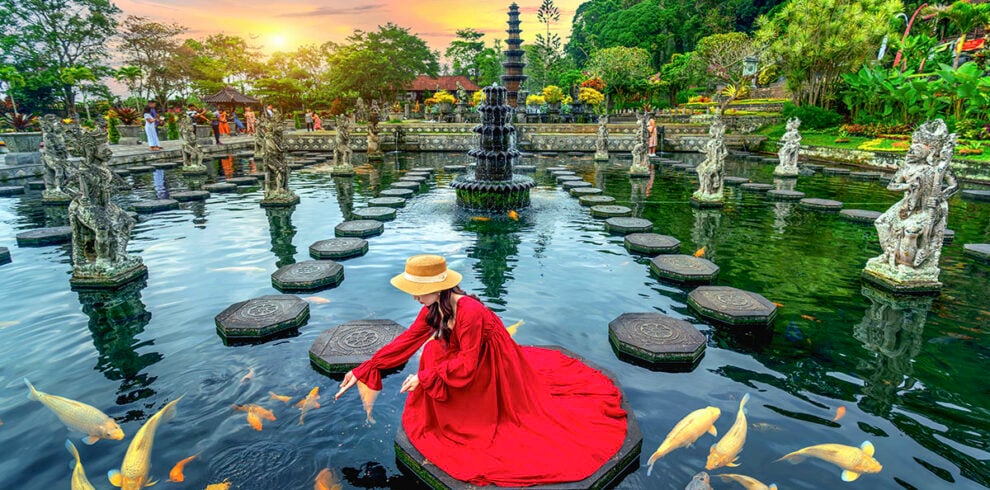 Vrouw voert kleurrijke vissen in de vijver van de Tirta Gangga op Bali