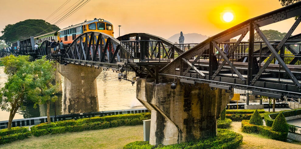 Een trein rijdt over de River Kwai Brug in Kanchanaburi bij zonsondergang