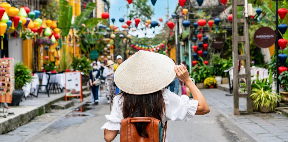 Vrouw met traditionele Vietnamese hoed loopt door de oude stad in Hoi An