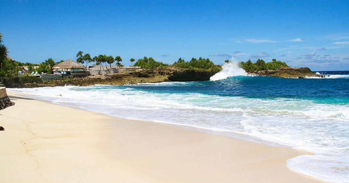 Rustig strand op Nusa Lembongan met witte golven en rotskust onder een heldere blauwe lucht