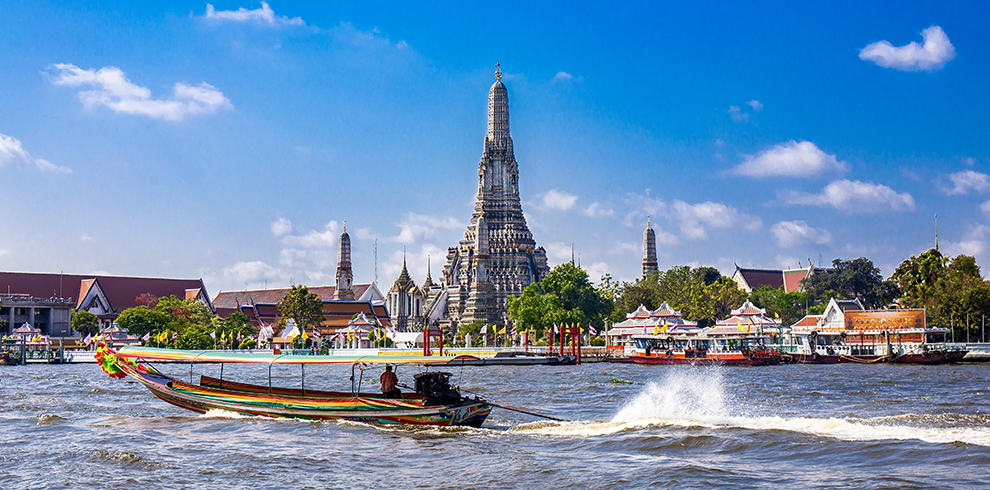 Een longtailboot op de Chao Phraya rivier met op de achtergrond de Wat Arun in Bangkok