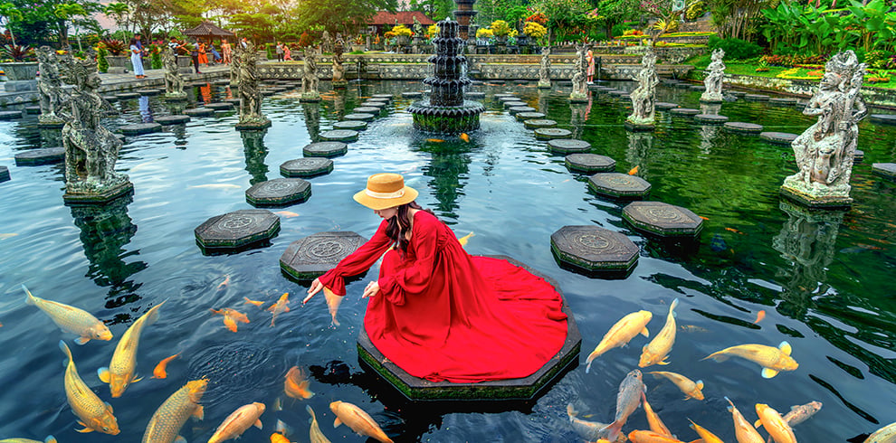 Vrouw voert kleurrijke vissen in de vijver van het Tirta Gangga Water Paleis op Bali