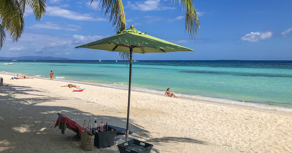 Toeristen ontspannen op het witte zand van White Beach (Dumaluan Beach) op Panglao Island, met helderblauw water en wuivende palmbomen.