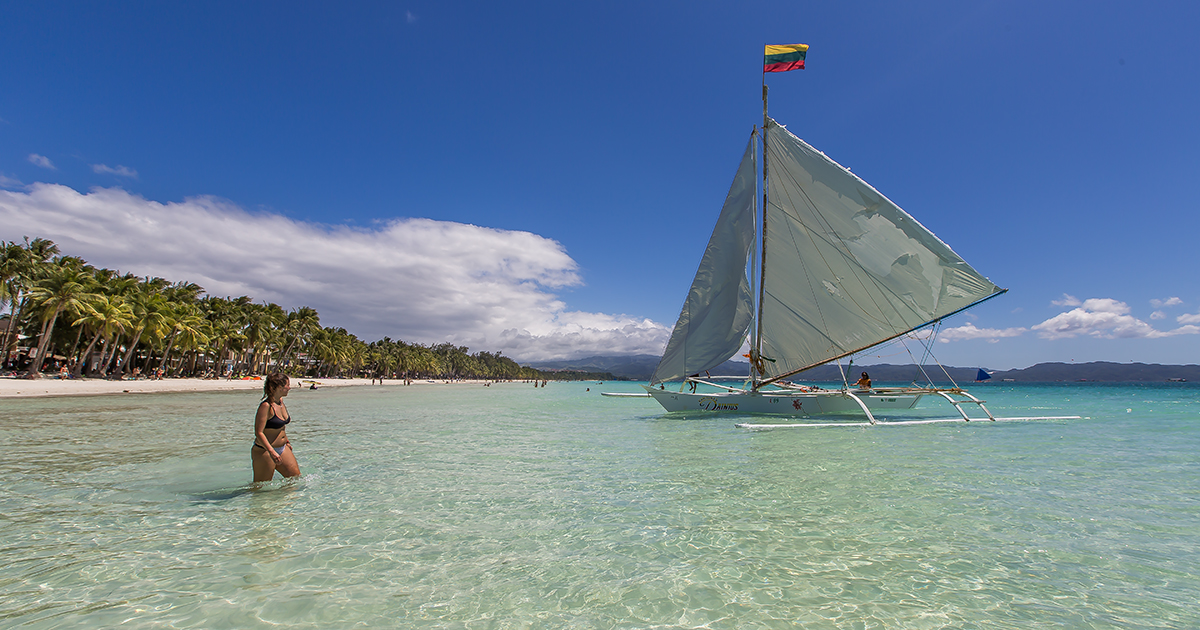 Vrouw in het zeewater voor de kust van Boracay, Filipijnen, met een traditionele Filipijnse paraw-zeilboot in beeld.