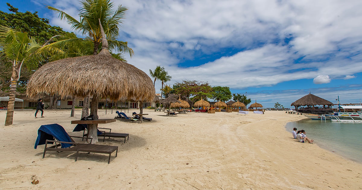 Tropisch strand op Mactan Island (Cebu) met parasols, ligbedden en uitzicht op de azuurblauwe zee.