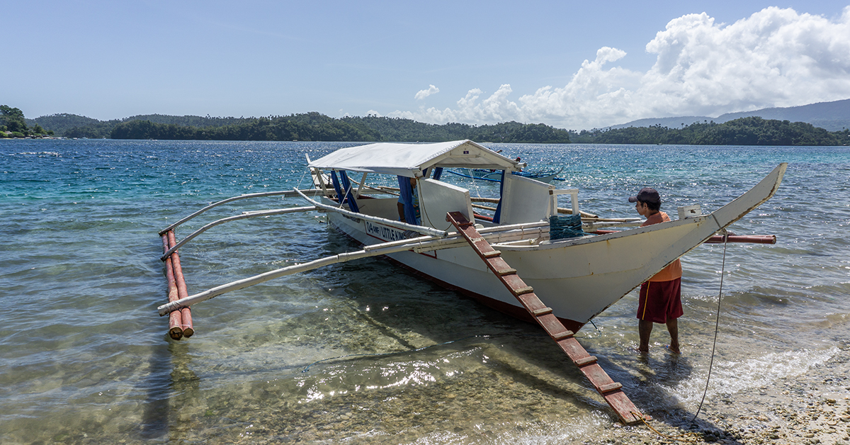 Man staat naast een traditionele Filipijnse boot aan de kust van Dumaguete, Filipijnen.