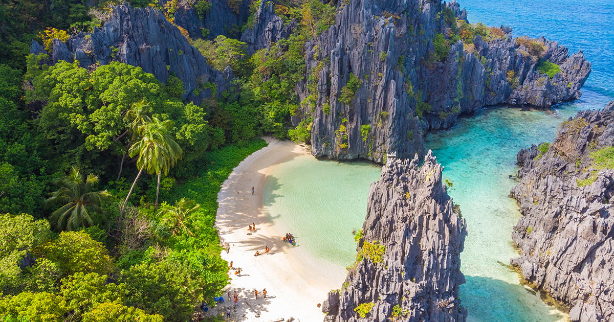 Luchtfoto van Hidden Beach op Matinloc Island, omringd door hoge kalkstenen kliffen en helder turquoise water bij El Nido, Palawan.