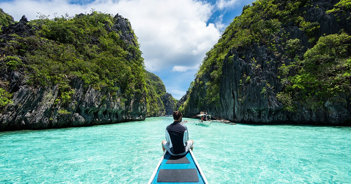Reiziger vaart op een traditionele boot langs de kalkstenen kliffen, turquoise lagunes en tropische eilanden van El Nido op Palawan.
