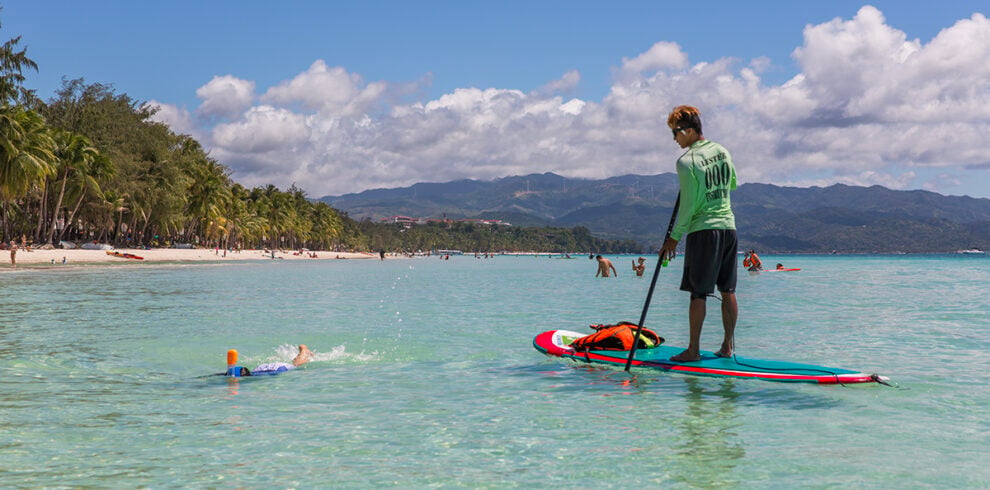 Man op een paddleboard terwijl iemand snorkelt in het heldere zeewater bij Boracay, Filipijnen.