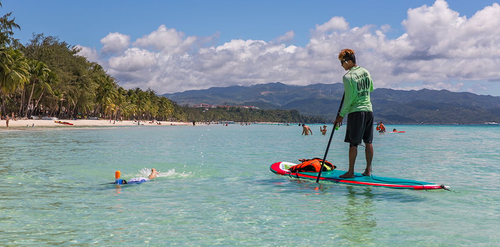 Man op een paddleboard terwijl iemand snorkelt in het heldere zeewater bij Boracay, Filipijnen.