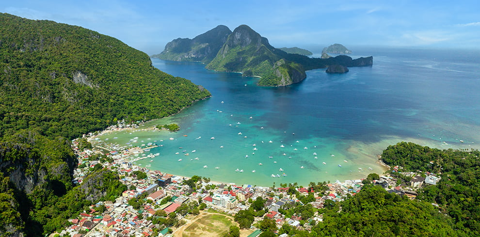 Panoramisch uitzicht op El Nido Town, omringd door tropische natuur en kleurrijke boten in de turquoise zee.