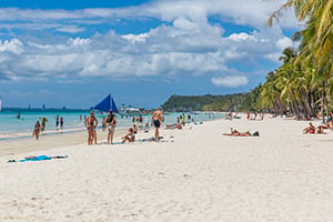 Mensen ontspannen op White Beach op Boracay, een tropisch strand met wit zand, palmbomen en helderblauw water.