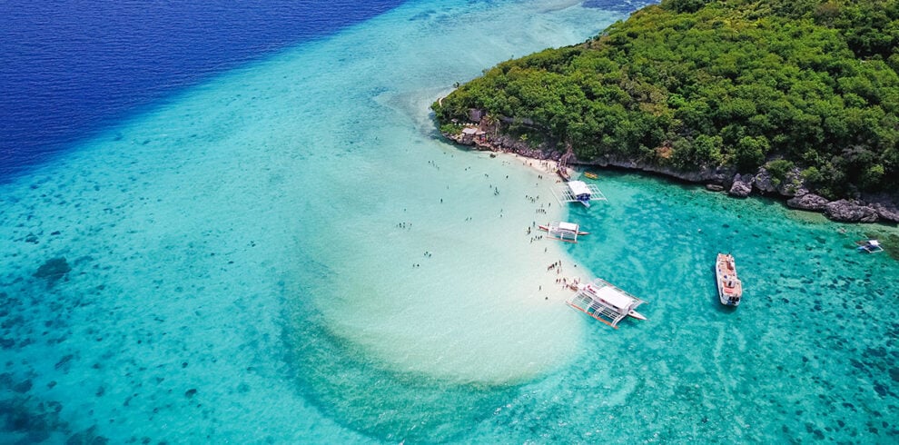 Luchtfoto van de zandbank op Sumilon Island met mensen in het water en traditionele bootjes in helder turquoise zee.