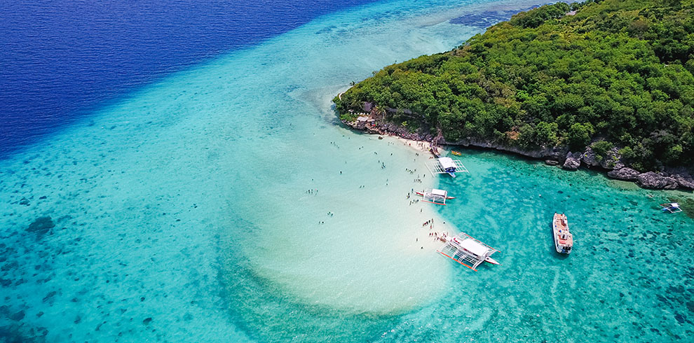 Luchtfoto van de zandbank op Sumilon Island met mensen in het water en traditionele bootjes in helder turquoise zee.