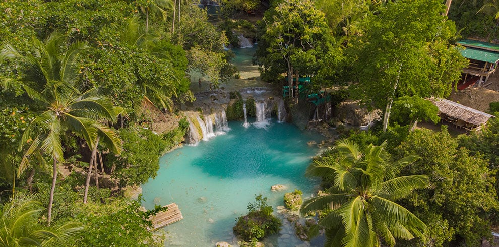 Luchtfoto van de Cambugahay Falls op Siquijor, met turquoise natuurlijke poelen, tropische begroeiing en watervallen die trapsgewijs door de jungle stromen.