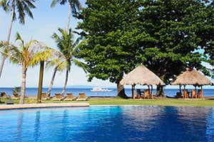 Zwembad bij Pura Vida Beach and Dive Resort met uitzicht op zee, omringd door palmbomen en tropische tuinen aan de kust van Dauin.