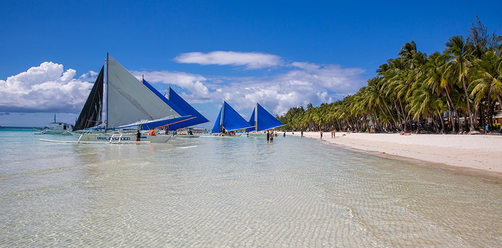 Bootjes en toeristen in het kraakheldere water bij White Beach, Boracay